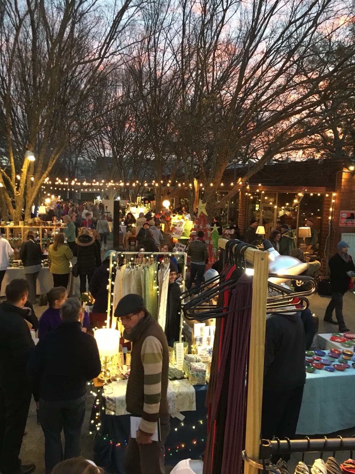 Shoppers browsing artist booths strung with lights in the Big City Bread courtyard at dusk